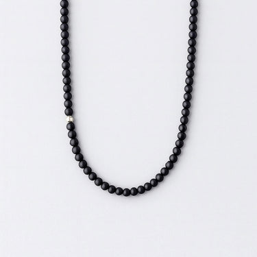 A strand of 4mm matte black onyx beads with a single off-centered sterling silver accent bead against a white background.
