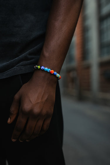 A close-up of a male model's wrist showcasing the vibrant, multi-colored details of an 8mm Millefiori glass bead bracelet.

