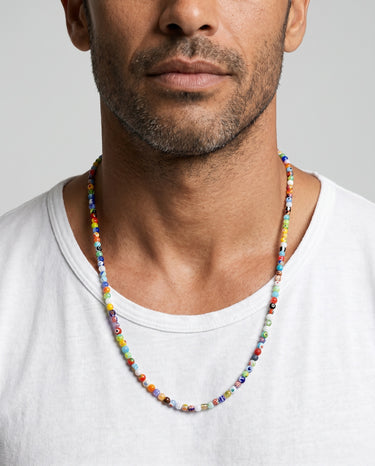 A close-up portrait of a male model in a white t-shirt wearing a single strand of 4mm colorful millefiori glass round bead necklace on a light gray background.