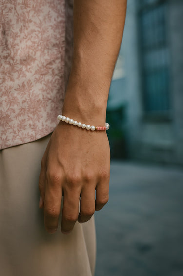 A lifestyle shot of a male model wearing a baroque pearl and rhodonite bracelet, demonstrating its slim profile and versatile summer aesthetic.
