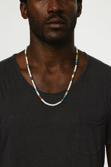 A male model wearing a black t-shirt showcasing the eclectic, multi-tonal look of a mixed gemstone heishi bead necklace.
