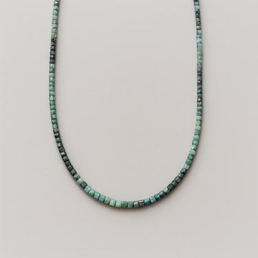 A strand of 3mm faceted green and teal tourmaline cube beads displayed in a U-shape against a neutral background.
