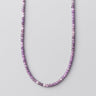 A polished purple Amethyst bead necklace displayed in a U-shape against a light grey background.

