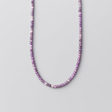 A strand of polished purple Amethyst beads displayed in a U-shape against a light grey background.
