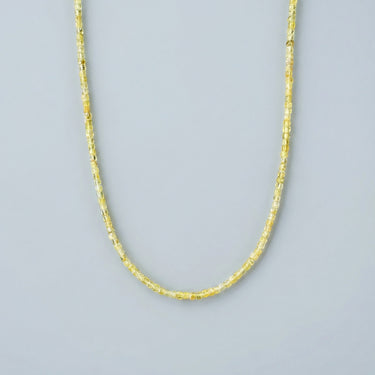 parial view of a peridot faceted 2mm bead necklace on a light gray background