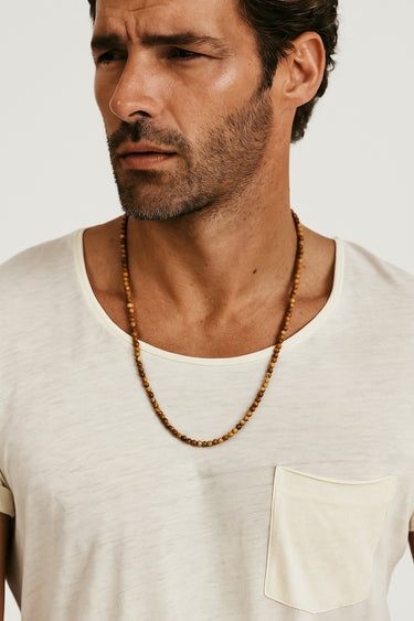 A male model wearing a white pocket t-shirt showcasing the natural tan and brown patterns of a 4mm picture jasper necklace.

