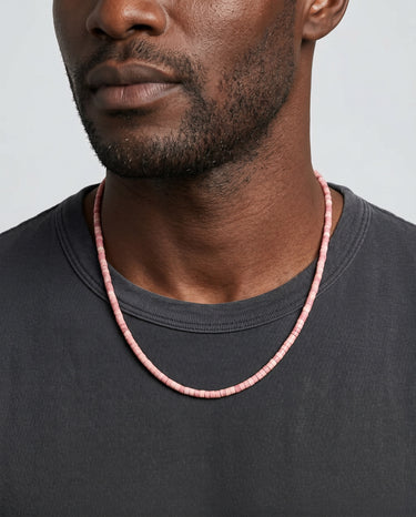 Man wearing a pink rhodonite heishi beaded necklace against a plain background