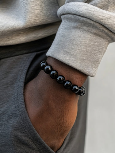 A male model's hand in his pocket, highlighting the sleek, deep black tones and light-reflecting polish of an 8mm onyx bracelet.
