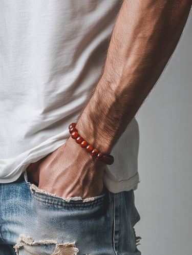 A close-up of a male model's wrist showcasing the bold 8mm scale and warm, translucent red tones of an Agate round bead bracelet.
