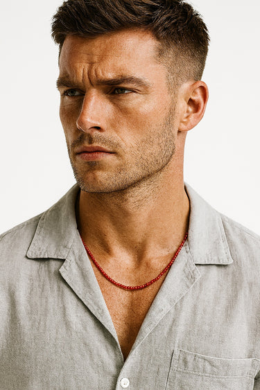 A male model wearing a light grey button-down shirt showcasing the bold color of a 4mm red agate beaded necklace.
