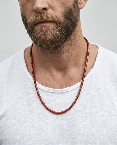 Man wearing a red beaded necklace against a plain background