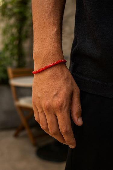 A close-up of a male model's wrist showcasing the bold red tones of a 4mm agate heishi bracelet against a black sleeve.

