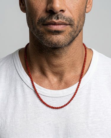 A close-up portrait of a male model in a white t-shirt wearing a 4mm red agate round bead necklace on a light gray background.
