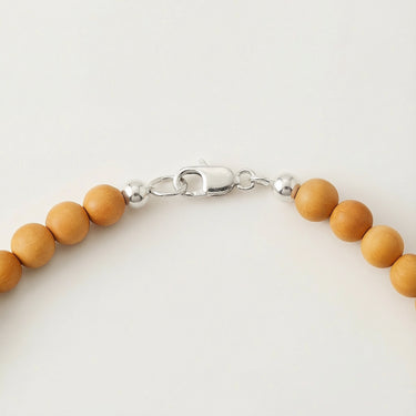 Close-up of a men’s necklace with 6mm round golden sandalwood beads and a polished sterling silver lobster clasp.
