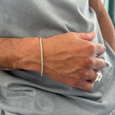 A lifestyle shot of a male model wearing a 2.5mm sterling silver chain bracelet, highlighting its slim, reflective profile against a grey t-shirt.
