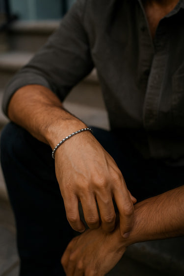 A lifestyle shot of a male model wearing a 3mm sterling silver rice bead bracelet, showcasing its slim profile and reflective finish.
