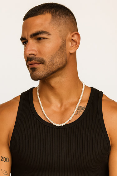 A man in a black ribbed tank top wearing a strand of 4-5mm white freshwater pearls.
