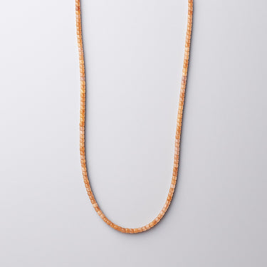 A strand of golden orange faceted sunstone beads hanging in a U-shape against a light grey gradient background.
