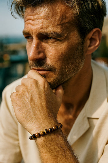 A lifestyle shot of a male model wearing an 8mm Tiger's Eye bracelet, highlighting the stone's natural chatoyancy and warmth.
