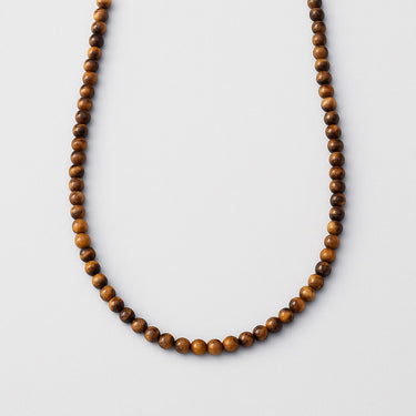 A single necklace of 6mm golden-brown Tiger's Eye beads displayed in a U-shape against a neutral light grey background.
