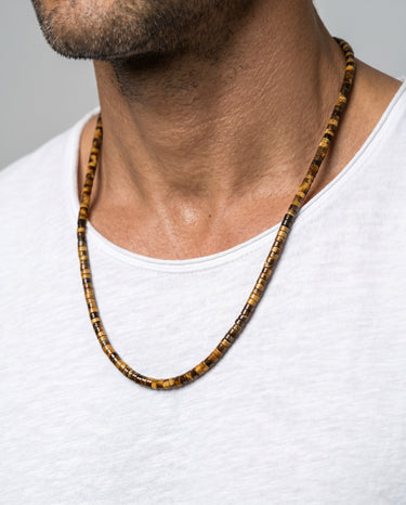 Man wearing a tiger's eye heishi beaded necklace on a plain background