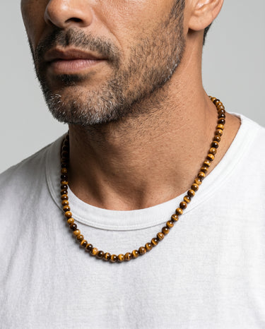 Men’s 6mm tiger’s eye bead necklace featuring natural tiger’s eye gemstone beads worn with a light gray crew neck shirt.