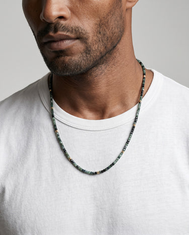 Man with white t-shirt wearing a tourmaline faceted cube beaded necklace with 14k gold-filled spacer accents against a plain background