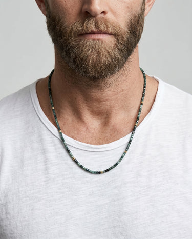 Man wearing a tourmaline faceted cube beaded necklace with 14k gold-filled spacer accents against a plain background