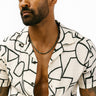 A Black male model wearing a white shirt with a black geometric pattern, showcasing a faceted tourmaline cube necklace with gold-filled spacers.
