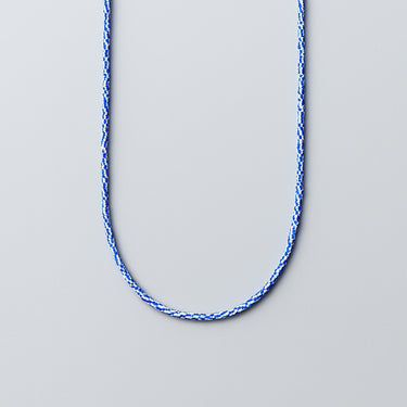 A strand of vintage blue and white layered chevron glass beads displayed in a U-shape against a neutral light grey background.
