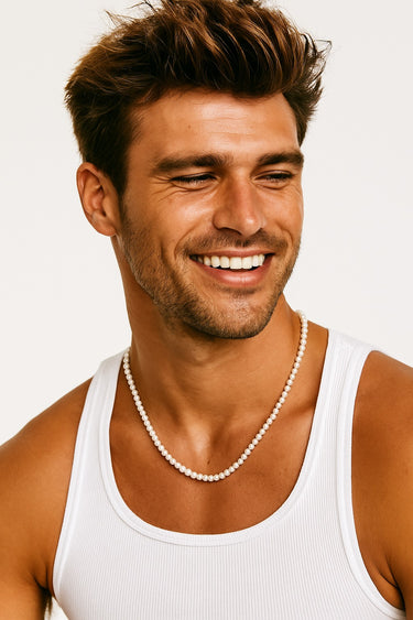 A smiling man in a white tank top wearing a subtle strand of 4-5mm white pearls.

