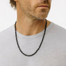 Man wearing a handcrafted Black Onyx necklace featuring 2–3mm faceted cube beads with polished surfaces and deep black tones, styled along the neckline.