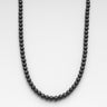A 4mm porous black lava beads necklace displayed in a U-shape against a neutral light grey background.
