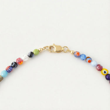 A close-up detailed shot focusing on a high-polish gold lobster clasp attached to a strand of 4mm multi-colored Millefiori glass beads against a white background.
