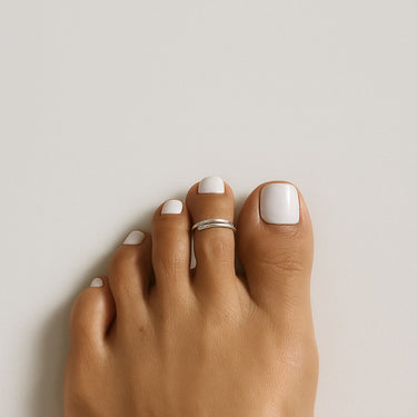 Toe with white nail polish and a silver ring on a neutral background