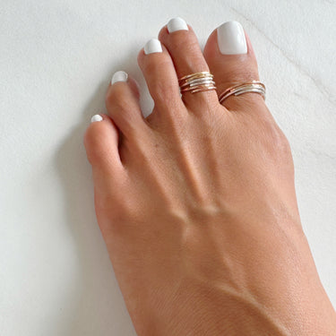 Foot model wearing adjustable stacked toe rings. Stacked mini toe rings. Stacked big toe rings. 14K Rose-Gold Filled and Gold filled. Slightly hammered to give texture and style.
