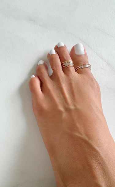 Foot model wearing adjustable stacked toe rings. Stacked mini toe rings. Stacked big toe rings. 14K Rose-Gold Filled and Gold filled. Slightly hammered to give texture and style.
