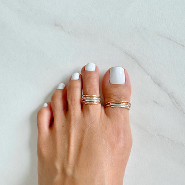 Foot model wearing adjustable stacked toe rings. Stacked toe rings. Stacked big toe rings. 14K Rose-Gold Filled and Gold filled. Slightly hammered to give texture and style.