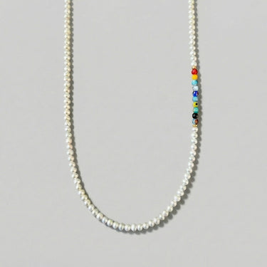 Product view of a handcrafted necklace featuring 4–5mm white freshwater pearls with an off-center arrangement of colorful Millefiori glass beads and small gold-tone accents against a light gray background.