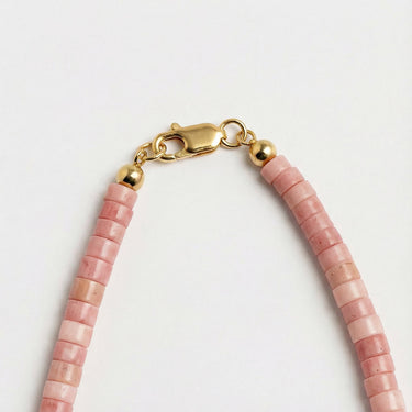 A close-up view of dusty rose Rhodonite heishi beads finished with a high-polish gold lobster clasp.
