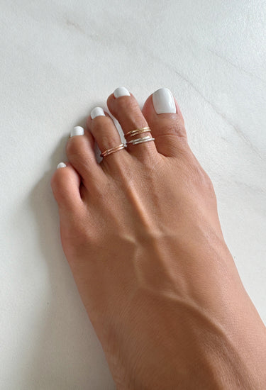 foot model wearing multiple overlap toe rings with white toe nail polish and soft white background