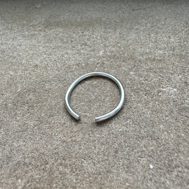 Silver anodized aluminum toe ring displayed on textured concrete surface — smooth metallic finish from the COLORS Collection.