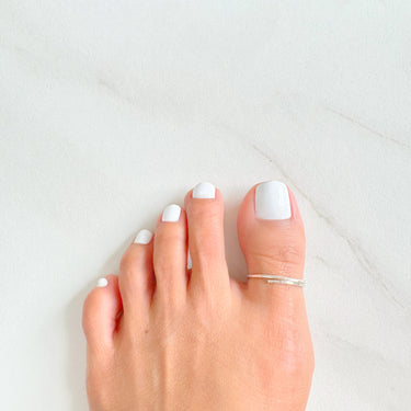 A silver BIG toe ring on a bare foot with white nail polish.