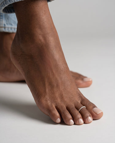 Close-up of a foot wearing a silver toe ring made with twisted rope wire on a neutral background