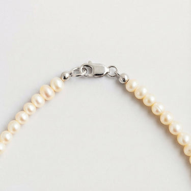 A macro close-up of small white pearls finished with a high-polish silver lobster clasp.
