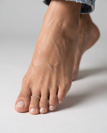 Close-up of a foot with a silver ring made of dotted wire on a neutral background
