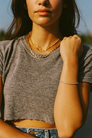A lifestyle shot of a model wearing the 2.5mm 14K gold-filled cube chain bracelet, highlighting its minimalist architectural silhouette and modern luxury appeal against a casual grey tee.
