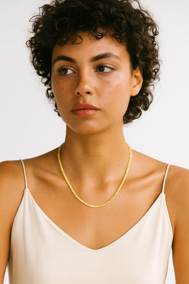 A woman wearing a 2mm faceted peridot cube necklace, highlighting the delicate scale and vibrant green glow of the architectural gemstone beads.
