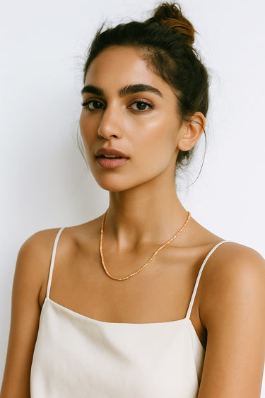 A close-up of a woman wearing a 2mm faceted golden orange sunstone cube necklace, showcasing the delicate scale and warm glow of the stones against her skin.
