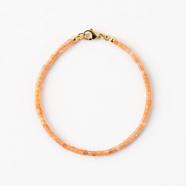A studio hero shot of a women's 2mm natural faceted golden sunstone cube bead bracelet with a 14K gold-filled clasp, highlighting the shimmering peach tones and delicate light-catching facets.

